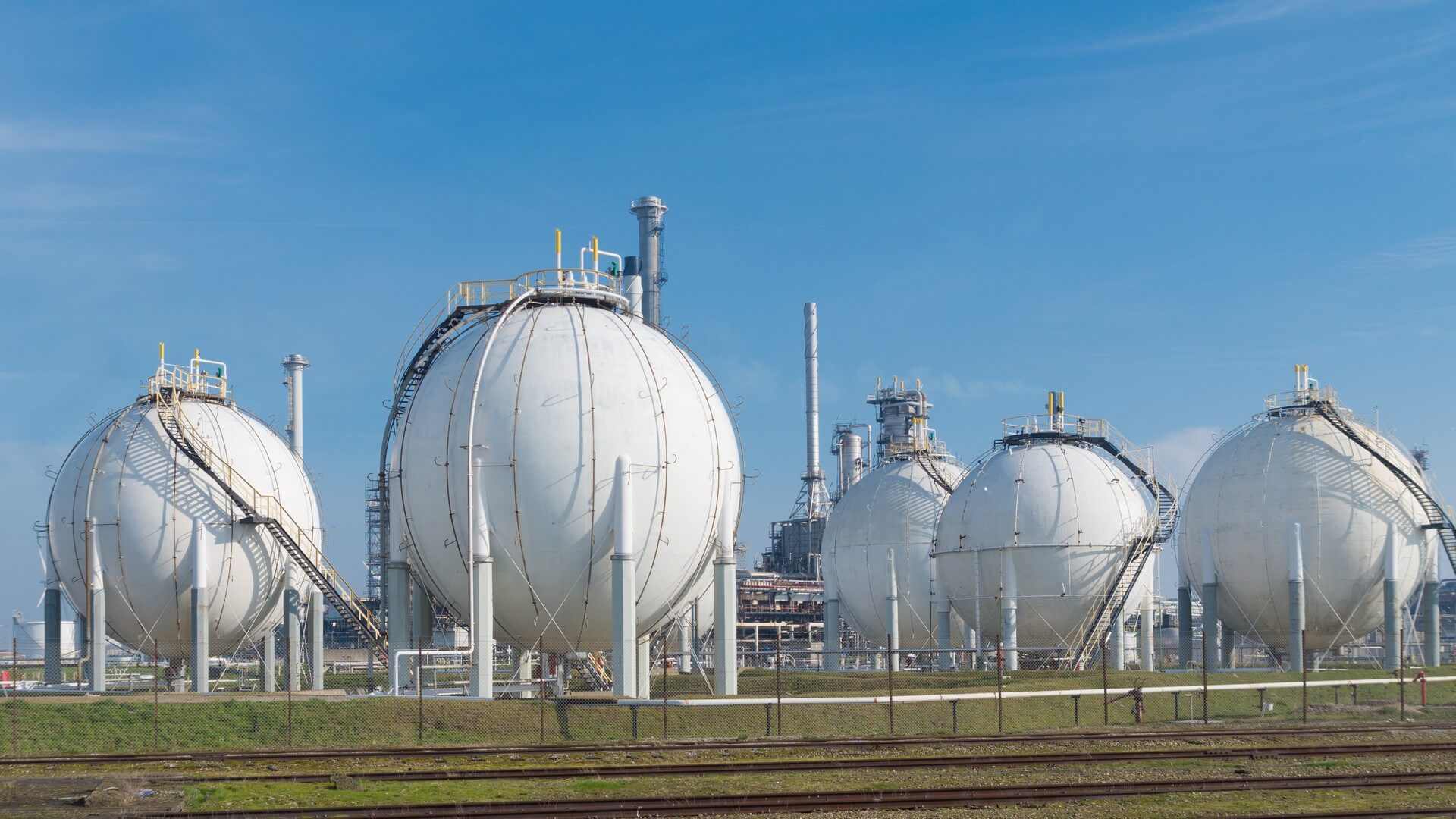 Three white gas tanks in a field with trees