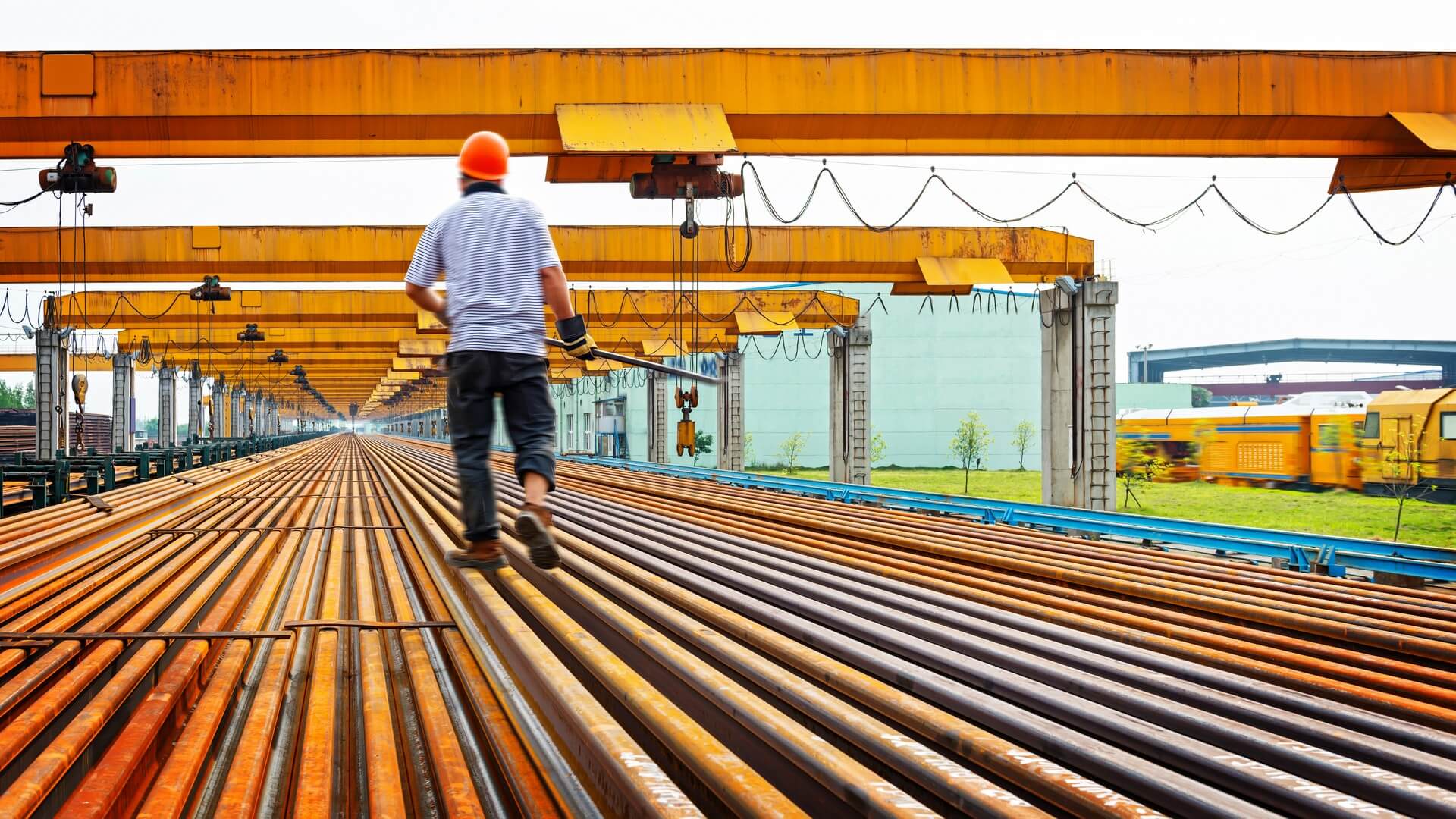A man in orange hard hat walking on train tracks.