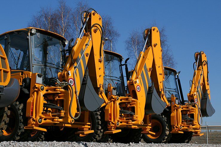 A group of yellow backhoes parked in front of some trees.