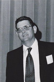 A man in suit and tie standing next to a curtain.